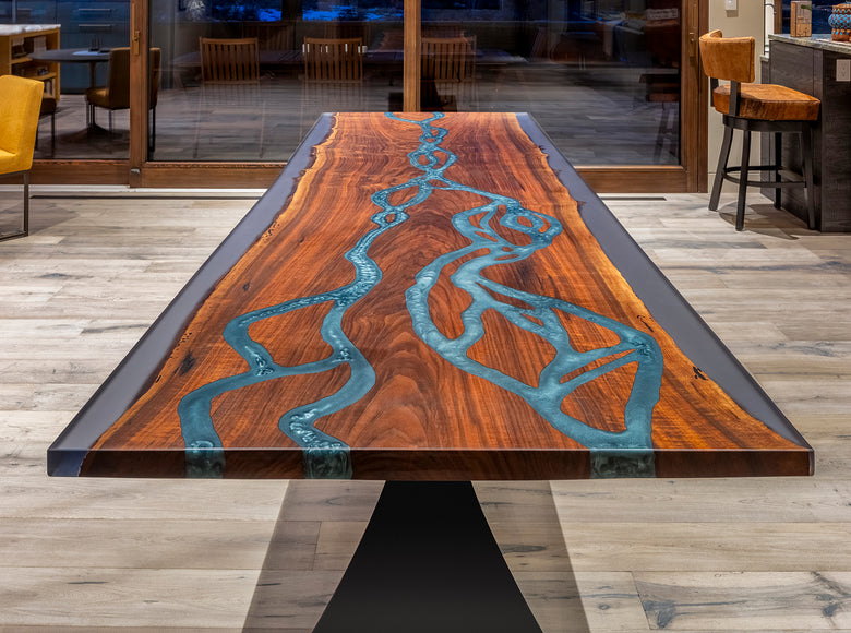 Wooden dining table with blue resin inlay and black metal base in a modern interior setting